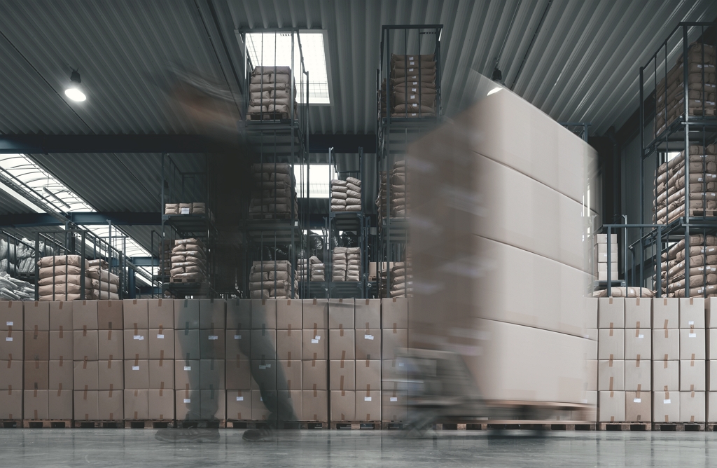 Halle mit Kartons und Mitarbeiter Mann zieht Kartons, im Hintergrund sind Kartons zu sehen.